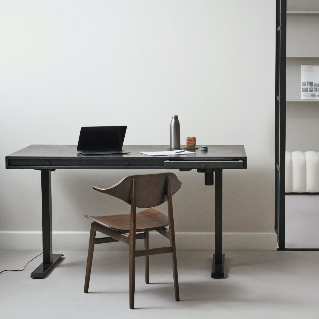 Modern adjustable desk for home office with laptop, water bottle, and small object in a minimalistic room.