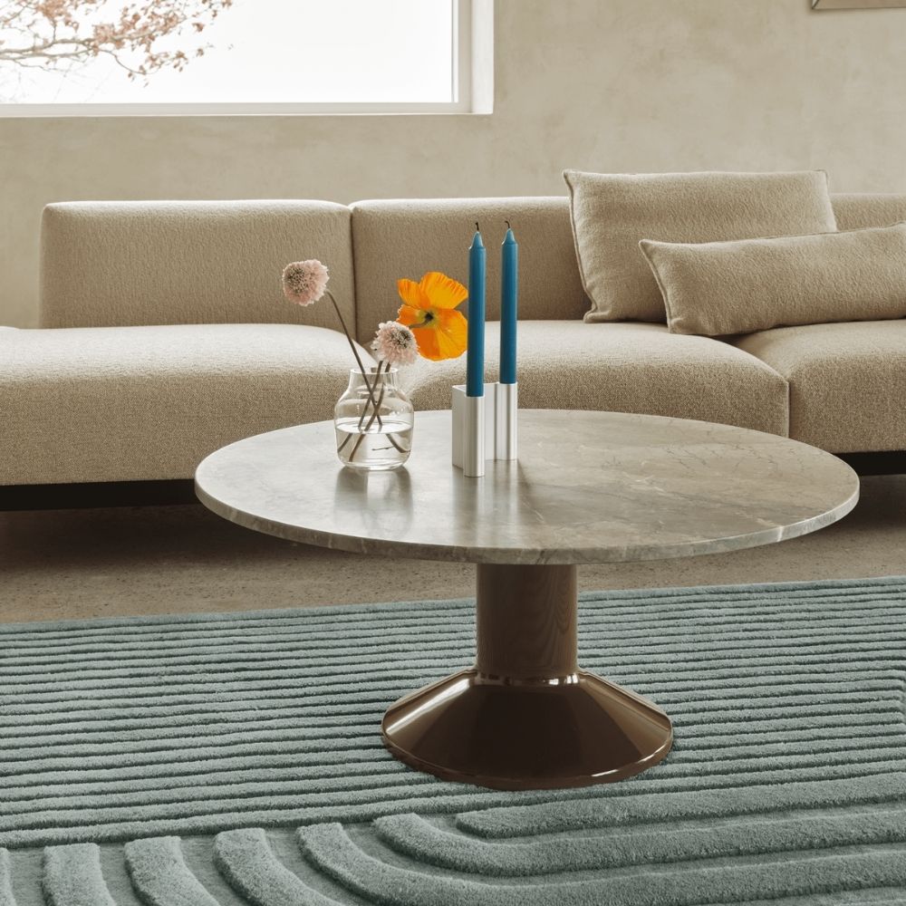 Midst Coffee Table, a round stone topped table supported by a bold column, shown in a living room