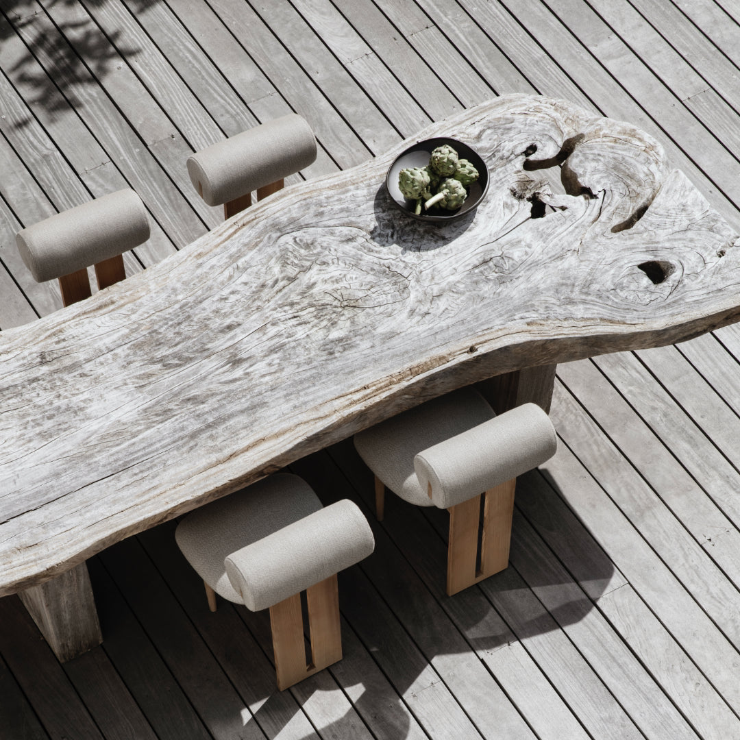 Wooden dining table with natural finish on a wooden deck, accompanied by stools.